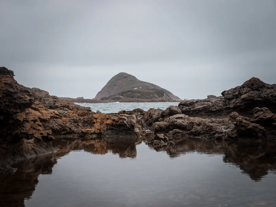 A calm rock pool reflecting a coastal island