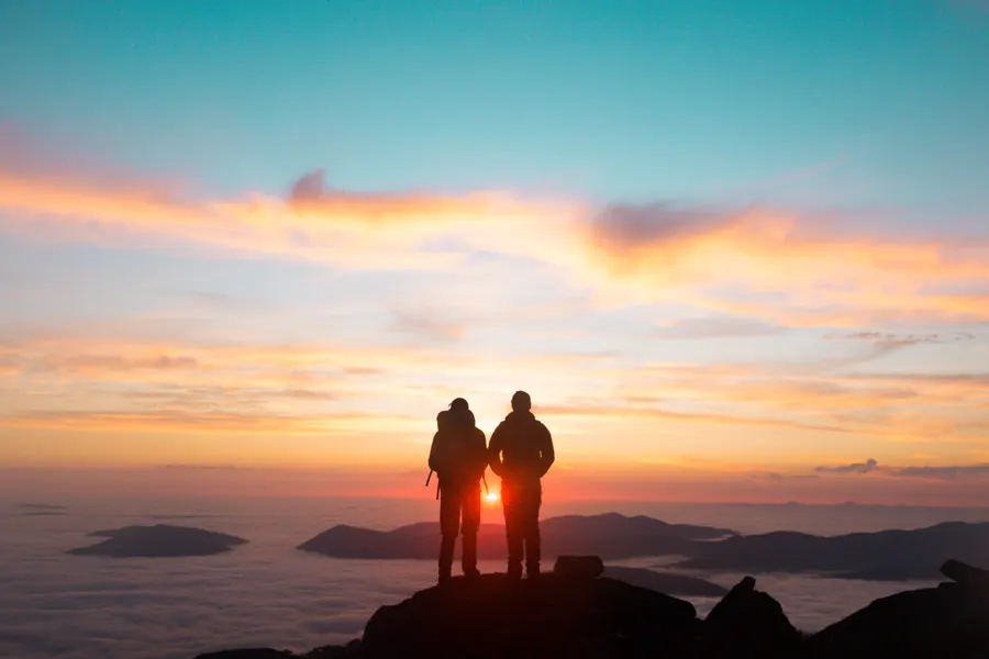 Two hikers above a sea of clouds at sunrise on an overnight adventure